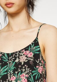 Camisola preta com estampado floral, com alças finas, apresentando impressões botânicas em rosa e verde e uma textura de tecido suave.