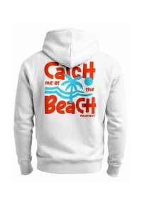 Weißer Hoodie mit grafischem Druck: roter und blauer Text "Fang mich am Strand" neben einer Palme und Wellen.