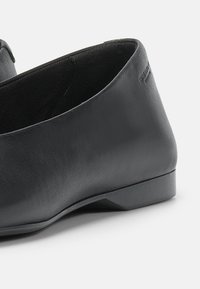 Chaussure noire en cuir à enfiler avec un petit talon et une finition lisse, vue de côté sur un fond clair.