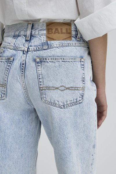 Svijetloplave traperice viskog struka, s vidljivim šavovima i stražnjim džepovima. Smeđi logotip na pojasu. Lagano istrošena tekstura.