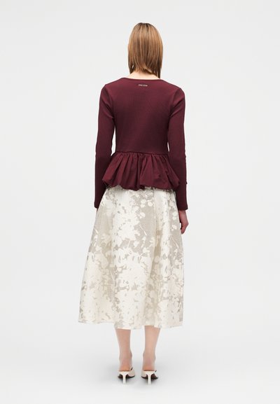 Bluza burgundie cu mâneci lungi și design peplum; asortată cu o fustă crem, până la genunchi, cu un model abstract și material texturat.