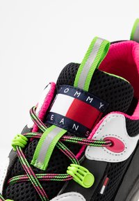 Sneaker nera con mesh e pelle sintetica, caratterizzata da accenti verde neon, interno rosa, lacci multicolore e logo Tommy Jeans.