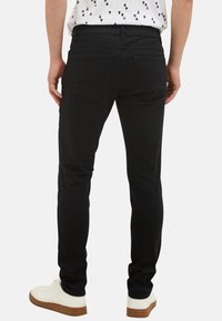 Černé džíny z denimu s úzkým střihem, standardními kapsami a jemnými detaily přišívání. V kombinaci s bílými teniskami.