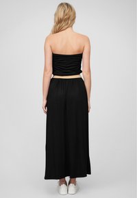 Svart stroppeløs topp med rynket design, paret med lange, flytende svarte bukser. Modellen har på seg hvite sneakers. Fokuser på enkelhet og komfort.