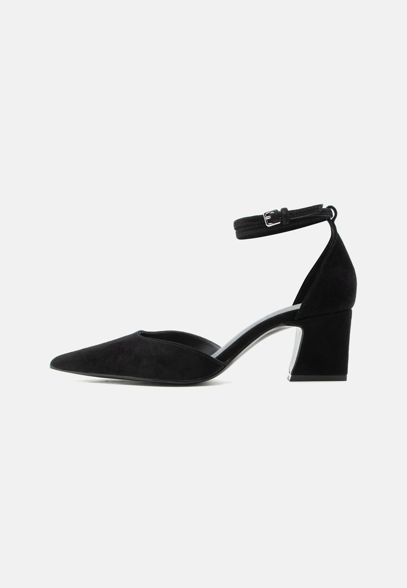 Chaussure pour femme en suède noir à bout pointu, talon bloc et bride de cheville avec boucle argentée, vue de côté sur fond blanc.
