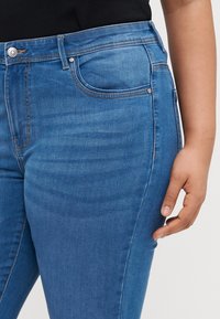 Blue denim jeans featuring a classic five-pocket design, light fading, and a subtle contrast stitching along the seams.