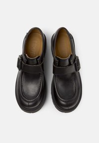 Chaussures en cuir noir avec un bout arrondi, une bride à boucle sur le dessus et une semelle en caoutchouc texturée. Fini lisse avec des coutures contrastantes.