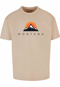 Béžové bavlněné tričko s grafikou hory a oranžovým sluncem, pod kterým je v černé barvě napsáno "MONTANA". Krátké rukávy, kulatý výstřih.
