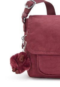Borsa a spalla in tessuto bordeaux con tracolla regolabile e un morbido portachiavi a forma di gorilla bordeaux appeso di lato.
