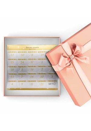 Boîte cadeau rose avec un nœud, ouverte pour révéler un calendrier en argent avec des accents dorés et des compartiments numérotés. Texte : "Secret Jewels by MYC Paris."