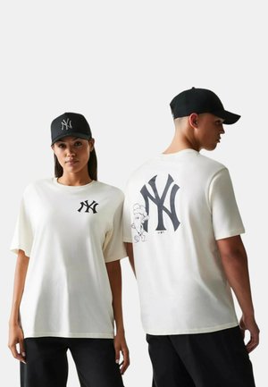Dos modelos con camisetas blancas de los New York Yankees y gorras negras; logo frontal en la camiseta de la mujer, logo grande en la espalda y caricatura en la camiseta del hombre.