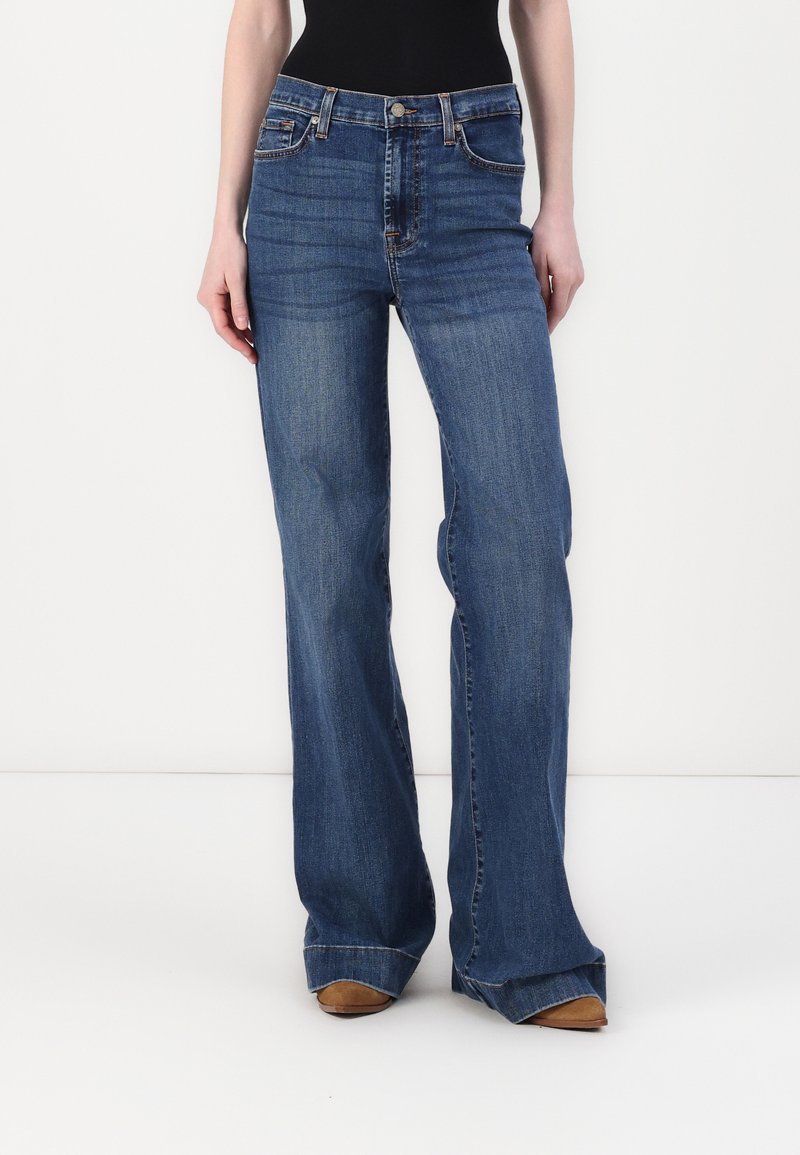 Bredde blå jeans med middels høyde i livet, fem lommer, og en falmet finish, laget av denim med synlige sømdetaljer.