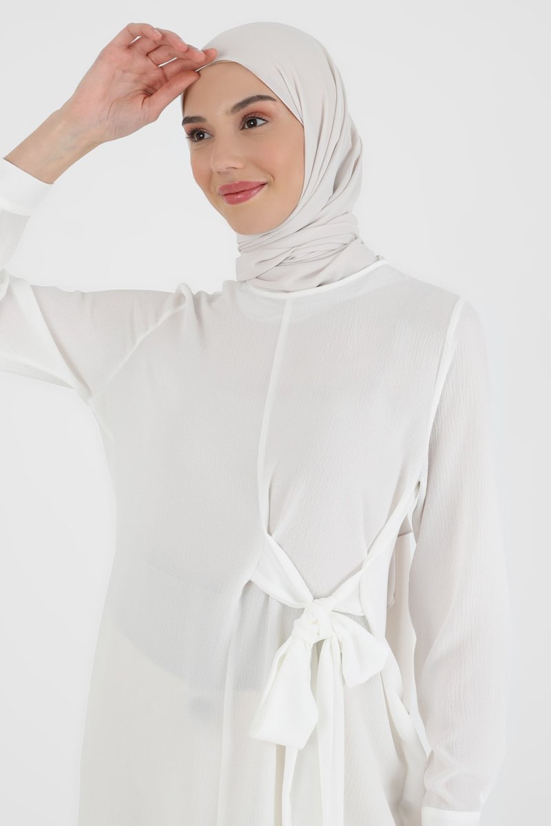 White chiffon dress with long sleeves, tied at the waist with a bow. Complemented by a light-colored hijab. Smooth texture, minimalistic design.