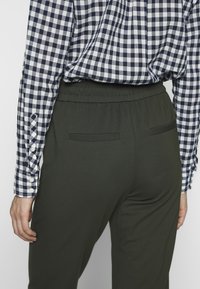 Nahaufnahme einer Person, die schwarze elastische Hosen und ein schwarz-weiß kariertes Langarmhemd trägt, von hinten gezeigt.