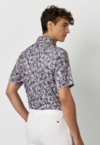 Kurzarmhemd in Marineblau mit einem hellen Blumenmuster, ausgestattet mit einem klassischen Kragen und einem strukturierten Stoff. Weiße Hose mit detaillierter Rückseite.