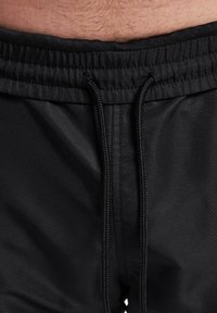 Shorts sportivi negri cu o finisare texturată, având o talie elastică, un șnur de ajustare și fără buzunare vizibile.