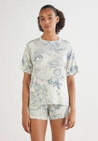 Baumwoll-Loungewear-Set mit einem cremefarbenen Oberteil und Shorts mit blauen Himmelsmotiven, einschließlich Planeten und Blumenmustern. Kurzärmlig, lässige Passform.