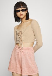 Top cropped canelado de cor bege clara com um laço central. Calções suaves com manchas rosa, apresentando uma cintura elástica e detalhes de cordão.