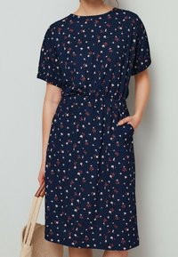 Námořnicky modré šaty s květinovým vzorem, krátkými rukávy, elastickým pasem a bočními kapsami. Vyrobené z jemné tkaniny s volným střihem.