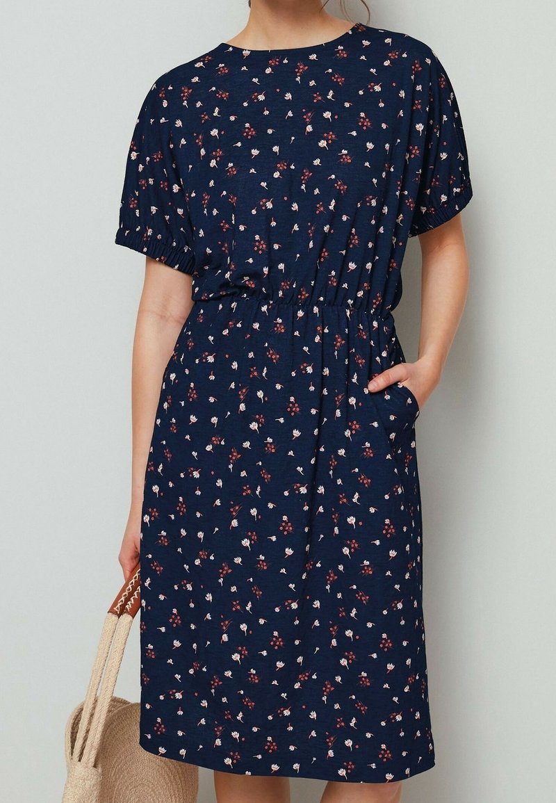 Námořnicky modré šaty s květinovým vzorem, krátkými rukávy, elastickým pasem a bočními kapsami. Vyrobené z jemné tkaniny s volným střihem.
