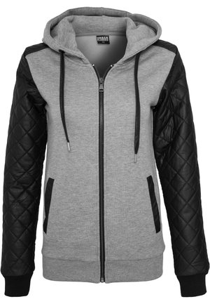 Sweat à capuche gris zippé avec une manche droite en simili cuir noir matelassé, poignets élastiques et poches avant. Capuche avec cordon de serrage et tissu lisse.