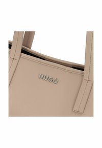 Sac fourre-tout en cuir beige avec le logo "HUGO" en relief ; texture lisse, forme structurée et deux anses allongées pour le transport.