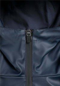 Acercamiento del zipper de una chaqueta azul marino con un detalle de calavera y huesos cruzados en la pestaña del tirador.