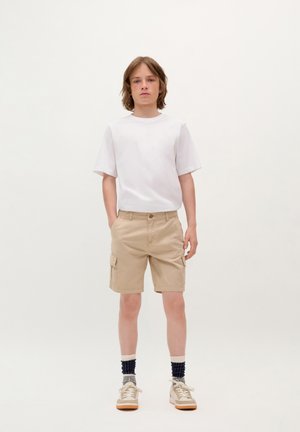 Witte t-shirt met korte mouwen, lichtbeige cargoshorts met zijzakken, gecombineerd met beige sneakers en gestreepte sokken. Eenvoudige, casual outfit.