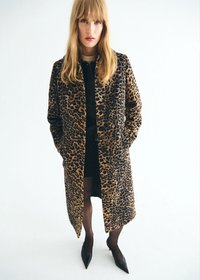 Cappotto con stampa leopardata, dalla consistenza morbida, maniche lunghe e taglio dritto. Indossato sopra un vestito nero e abbinato a tacchi a punta neri.