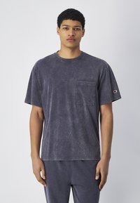 Camiseta de manga corta en gris oscuro, hecha de algodón, con un bolsillo en el frente, escote redondo y una textura desgastada. Logo en la manga izquierda.