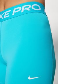 Leggings Nike Pro turquoise avec une large ceinture portant le texte "NIKE PRO", un tissu lisse et un logo Nike swoosh blanc sur la cuisse.