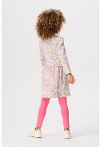 Robe à motifs floraux dans des teintes pastel avec des manches longues, taille cintrée et leggings roses. Portée avec des baskets de couleur claire.