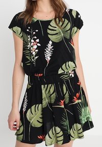 Schwarzes Kleid mit kurzen Ärmeln, das ein tropisches Blatt- und Blumenmuster in Grün, Weiß und Rot aufweist, mit einem elastischen Taillenbund und einem ausladenden Rock.