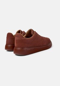 Sneakers in pelle marrone con una finitura liscia, punta arrotondata e suole in gomma. Presentano un branding discreto sul tallone e una foderatura beige.