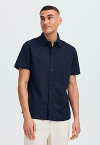 Camisa de botones de manga corta en un oscuro color navy, con cuello, hecha de una tela texturizada y que presenta una tapeta con botones a juego.