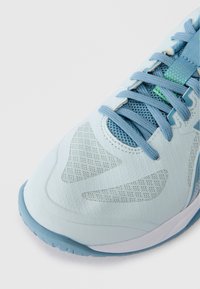 Ανοιχτό μπλε αθλητικό παπούτσι με δίχτυ, υφή στην επιφάνεια, μπλε κορδόνια και καουτσούκ σόλα, εικονιζόμενο από τη μπροστινή γωνιακή πλευρά.