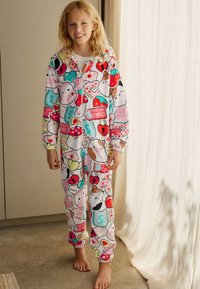 Tuta intera in pile in colori pastello con vari personaggi dei cartoni animati, cuori e motivi di cibo; include un cappuccio e polsini elastici su maniche e caviglie.