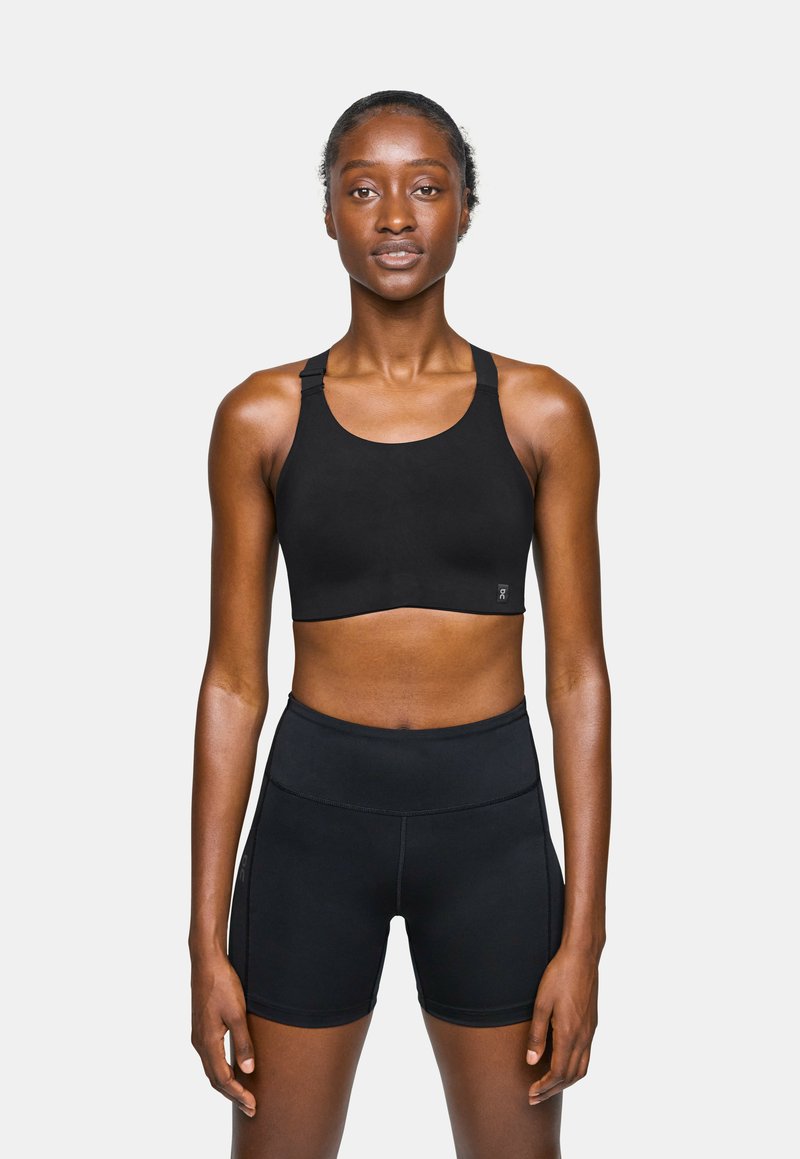Sujetador deportivo negro con tirantes anchos y escote redondo, combinado con pantalones cortos negros de cintura alta. Ambos están hechos de un material suave y elástico.