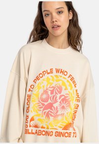 Cream-colored sweatshirt with a relaxed fit, featuring a colorful floral graphic and text in orange and yellow, made from soft fabric.