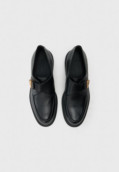 Čierne kožené topánky s textúrovaným povrchom, vybavené prekrytým remienkom a detailom z kovovej pracky. Zaoblená špička a pevná čierna podrážka.