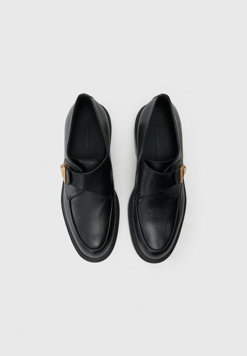 Scarpe in pelle nera con finitura testurizzata, caratterizzate da una fascia sovrapposta e dettaglio di fibbia in metallo. Punta arrotondata e suola nera solida.