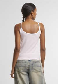 Svetloružové bavlnené tielko s tenkými ramienkami a hlbokým výstrihom na chrbte, v kombinácii s modrými džínsami s trhaným efektom a náprsnými vreckami.