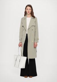 Light gray trench coat with double-breasted design, gold buttons, and wide lapels, paired with black wide-leg trousers and a white tote bag.