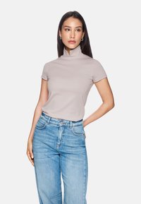 Short-sleeve, high-neck top in light beige fabric, paired with high-waisted light blue jeans. Smooth texture, simple design, and neutral colors.
