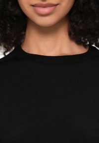 Μαύρο πλεκτό τοπ με ριμπ υφή και στρογγυλή λαιμόκοψη, που χαρακτηρίζεται από ομαλή υφή και εφαρμοστή γραμμή. Χωρίς εμφανή μοτίβα ή διακοσμήσεις.