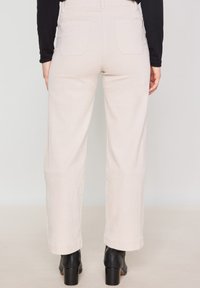 Lichtbeige corduroy broek met een rechte pijp, voorzien van twee achterzakken en gecombineerd met zwarte hoge hakken.