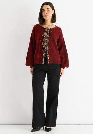 Burgundy sweater with a round neckline, featuring a leopard print tie detail. Paired with high-waisted black wide-leg pants and black heels.