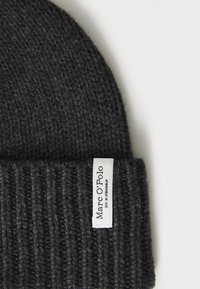 Berretto di lana nero lavorato a maglia con texture a costine e etichetta bianca con scritto "Marc O'Polo" e "EST. IN STOCKHOLM." Materiale morbido ed elastico.