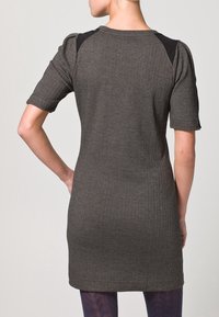 Pletené šaty v tmavě šedé barvě s herringbone vzorem, krátkými rukávy a černými akcenty na ramenech. Jednoduchý, těsně přiléhající silueta a strukturální látka.