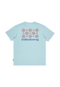 Vaaleansininen T-paita, jossa on kuvioitu malli takana punaisista, oransseista ja sinisistä muodoista, sekä "Billabong"-logo tummansinisellä.